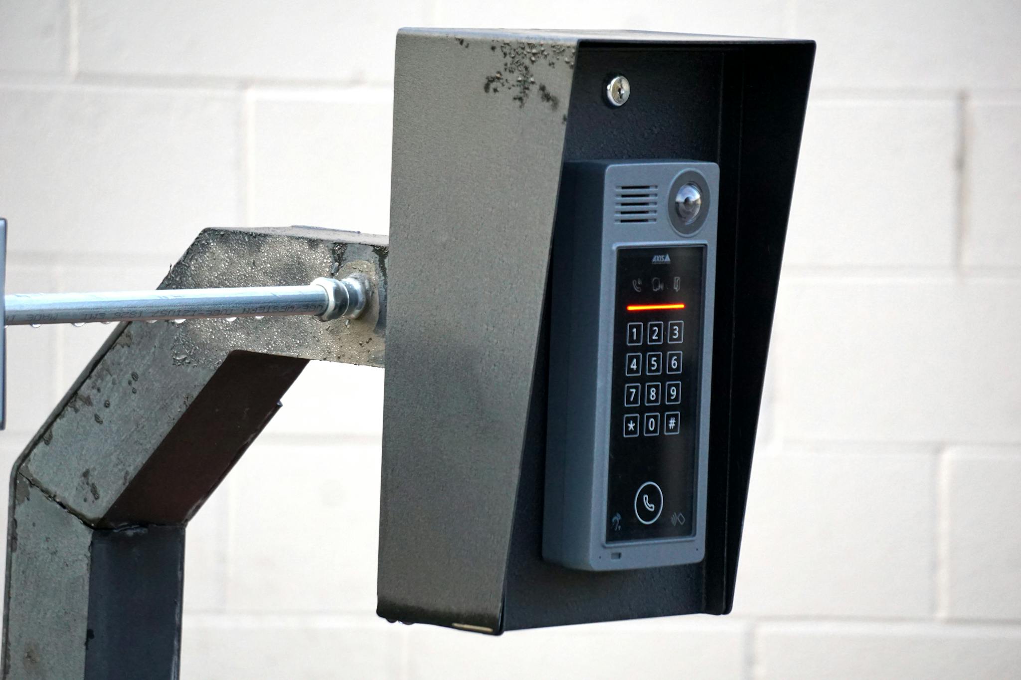 Close-up of a modern security intercom and keypad mounted on a wall outdoors with visible wiring.